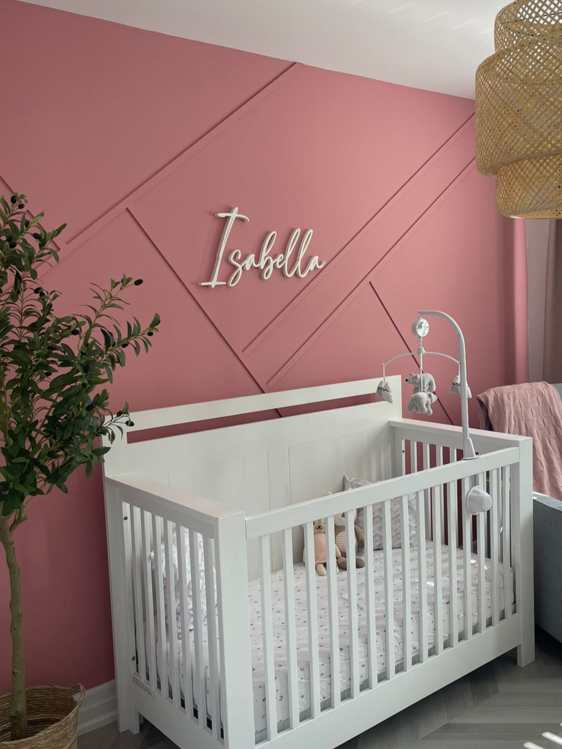 Nursery room with a white crib, pink wall, and decorative elements.
